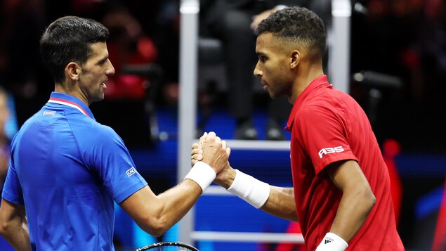 Les deux joueurs de tennis, Djokovic en bleu et Auger-Aliassime en rouge, se serrent la main au filet après la victoire de ce dernier. 