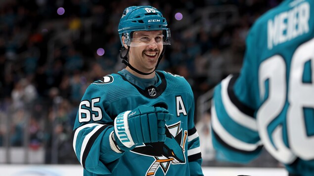 Un joueur de hockey, à l'uniforme turquoise, sourit en offrant le poing. 