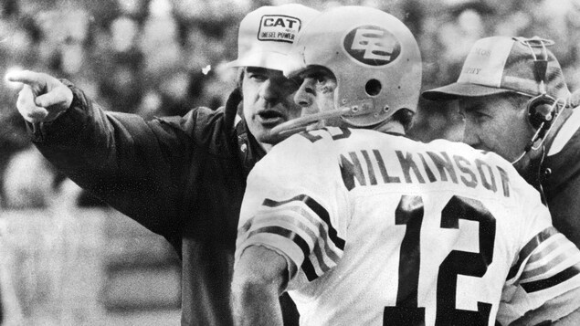 Photo en noir et blanc de 1978. Le quart arrière des Eskimos Tom Wilkinson reçoit les instructions de son entraîneur Hugh Campbell.