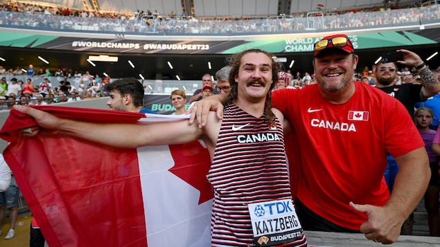 Un athlète pose avec son entraîneur. L'athlète tient le drapeau du Canada.