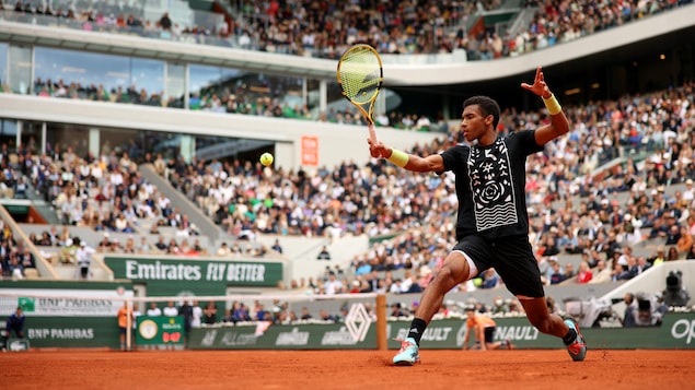 Un joueur de tennis vêtu de noir s'étire pour frapper une balle du revers lors d'un match à Roland-Garros. 