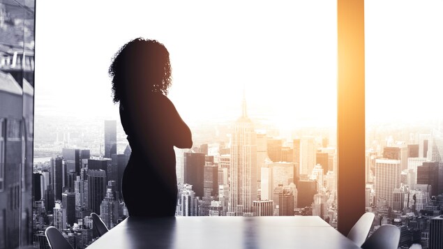 Une femme dans un bureau regarde par une grande fenêtre.