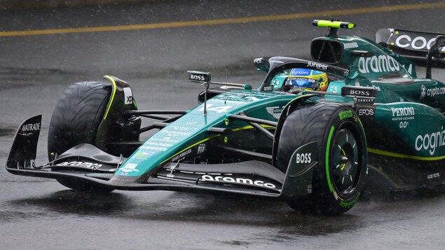 Une monoplace F1 roule sous la pluie en pneus rainurés sur un circuit urbain détrempé.