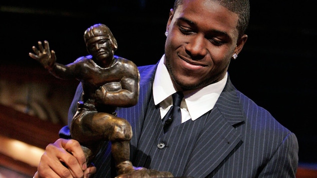 Un homme souriant regarde et tient un trophée à l'effigie d'un joueur de football.