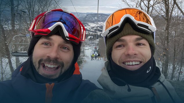 Deux skieurs regardent la caméra et sourient pendant qu'ils sont assis dans une remontée mécanique.