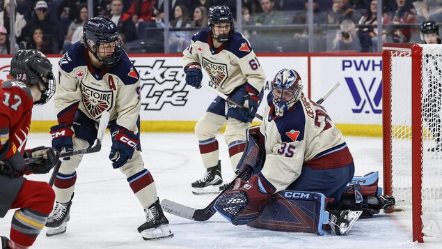 Une hockeyeuse marque un but contre une gardienne et deux rivales.