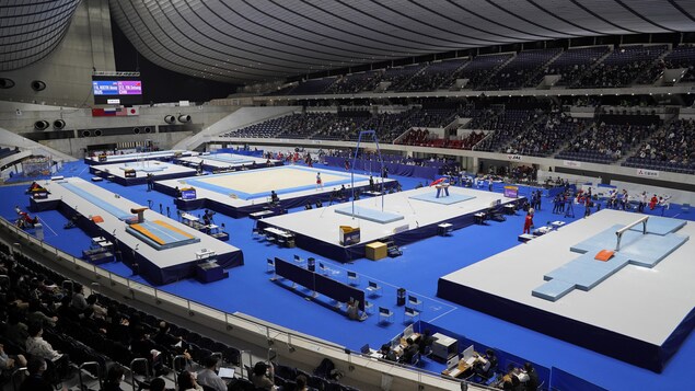 Vue d'ensemble d'un stade avec des spectateurs dans les gradins et de l'équipement de gymnastique au centre.