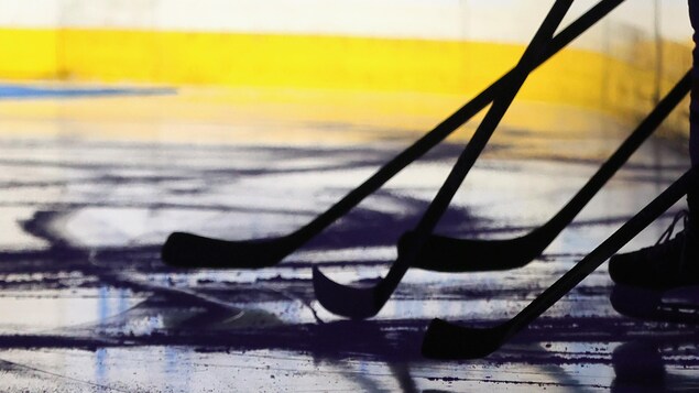On aperçoit les contours de plusieurs bâtons de hockey sur une patinoire.
