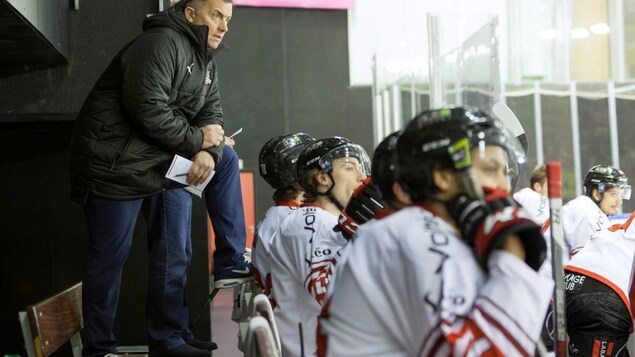 Il est derrière le banc rempli de joueurs lors d'un match en France.