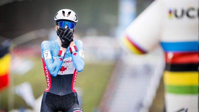 Une cycliste porte ses mains à son visage alors qu'elle passe la ligne d'arrivée la première d'une compétition.