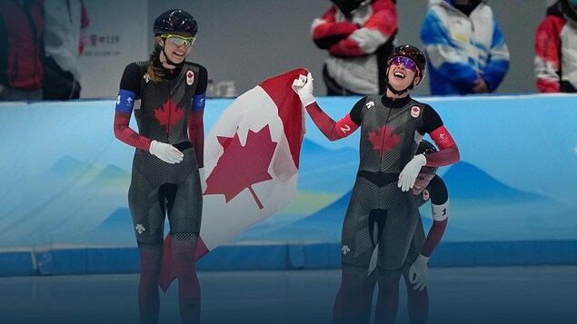 Deux patineuses de vitesse tiennent un drapeau canadien et sourient.