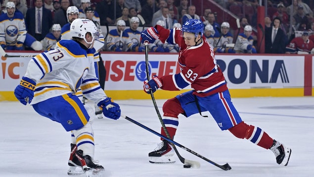 Sur une patinoire, deux joueurs de hockey se font face avec une rondelle entre les deux.