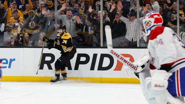 Un hockeyeur célèbre un but près de la bande, non loin d'un gardien.