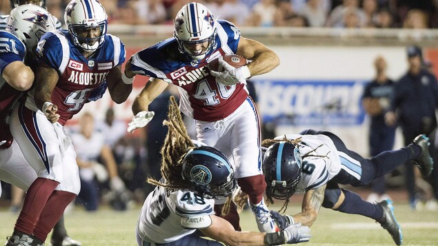Deux joueurs des Argonauts effectuent un plaqué contre Jean-Christophe Beaulieu. Deux joueurs des Argonauts effectuent un plaqué contre Jean-Christophe Beaulieu.