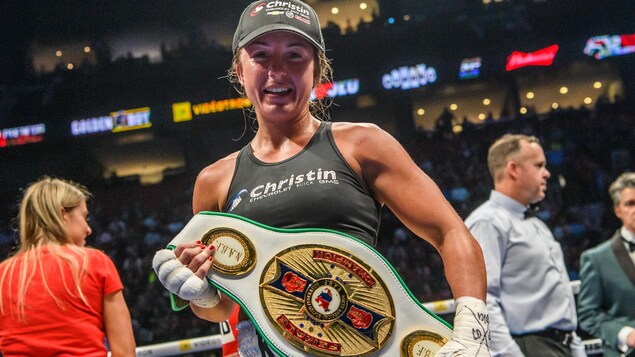 Une boxeuse souriante dans le ring tient sa ceinture de championne
