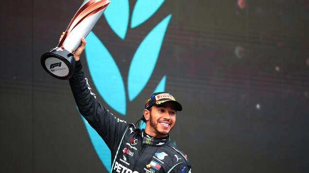 Le pilote automobile lève un trophée en souriant.