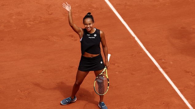 Une joueuse de tennis vêtue de noir salue la foule de la main après sa victoire sur la terre battue rouge du tournoi de Roland-Garros. 