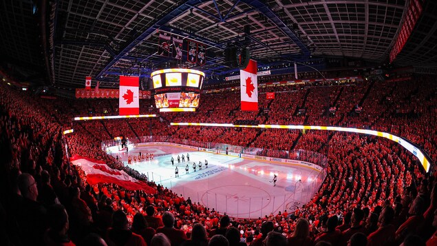 Un plan large d'un aréna de hockey bondé de spectateurs, avec un drapeau canadien à l'écran géant.