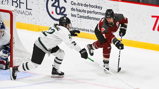 Deux joueuses de hockey d'équipes adverses tentent de maîtriser une rondelle, elles se trouvent à gauche du filet.