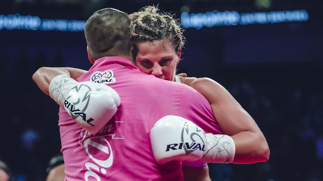 Une boxeuse et son entraîneur se serrent dans leurs bras sur le ring.