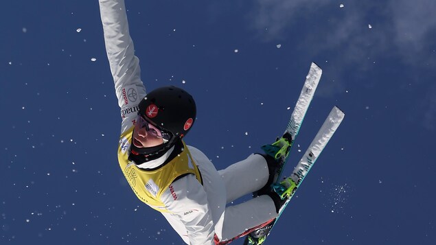 La skieuse effectue un saut, la tête à l'envers.