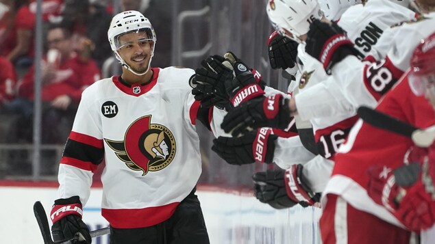Le hockeyeur Mathieu Joseph sourit en patinant devant ses coéquipiers qui sont installés au banc des joueurs.