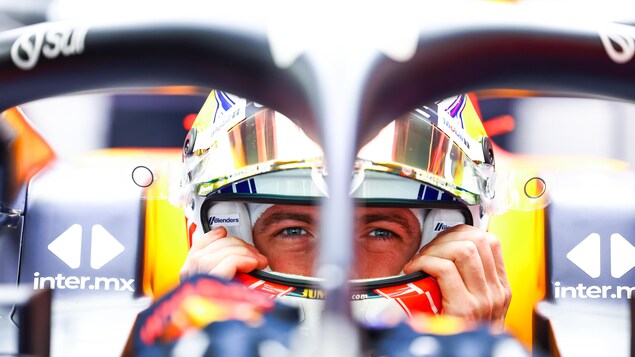 Le pilote néerlandais Max Verstappen, assis dans sa voiture Red Bull, installe son casque sur sa tête. 