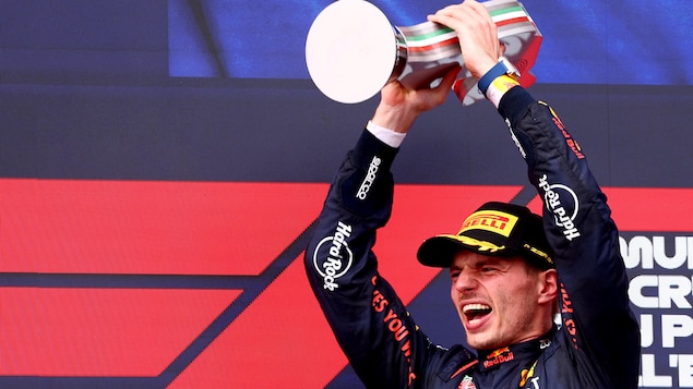 Un pilote de F1 soulève un trophée à deux mains et réagit, visiblement très heureux.