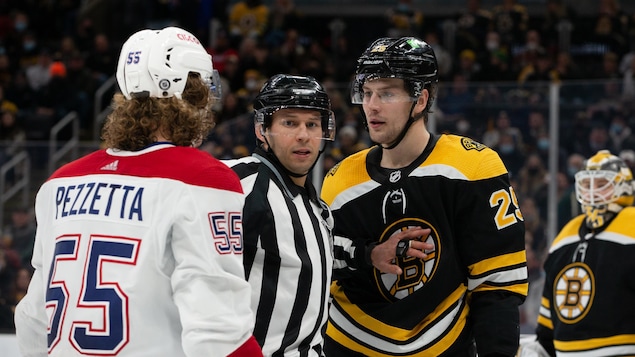 Deux joueurs de hockey sont séparés par un juge de ligne.