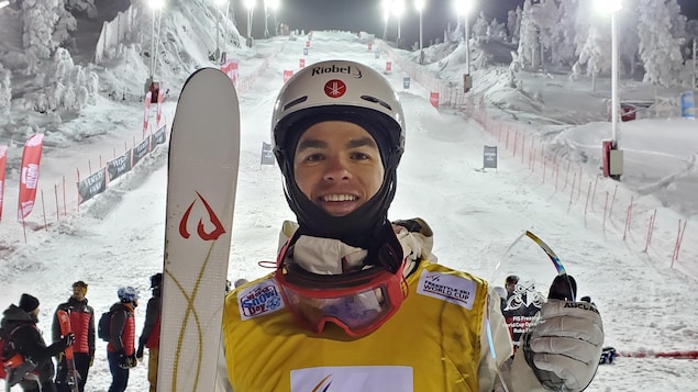 Un skieur acrobatique tient un trophée dans une main et il sourit.