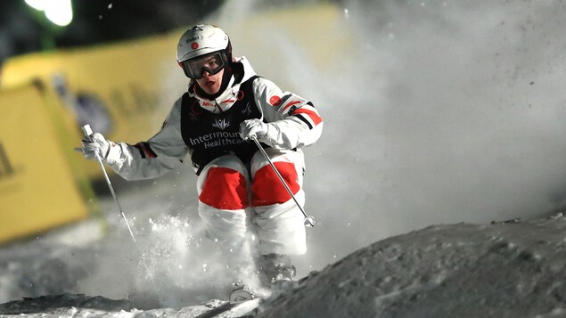 Il est en plein effort, les genoux pliés, dans une pente de ski.