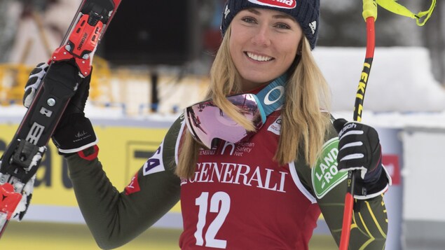 Elle sourit à la caméra, les skis en main.