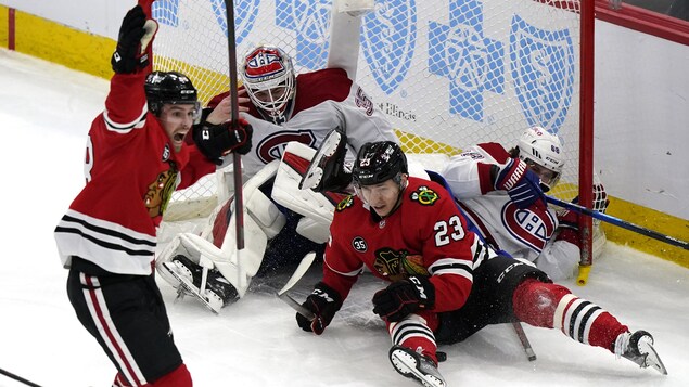 Trois joueurs sur la glace dans un filet décroché. Devant eux, un joueur en rouge lève les bras.