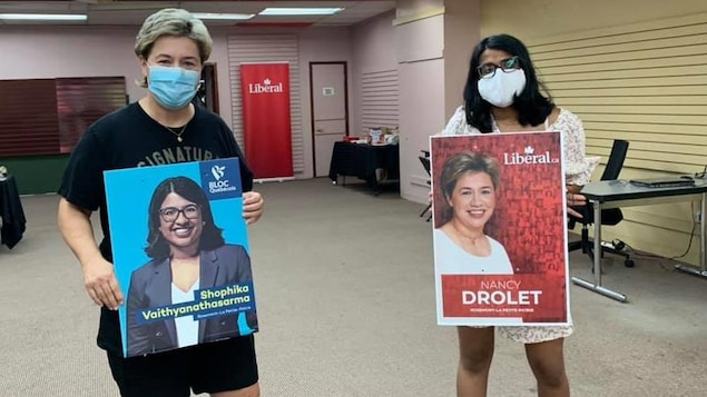 La liberal Nancy Drolet y el Bloc Québécois Shophika Vaithyanathasarma intercambian carteles electorales para una foto.