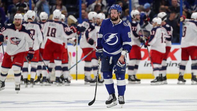 Déçu, Nikita Kucherov regarde dans le vide. Derrière lui, les joueurs des Blue Jackets célèbrent leur victoire.