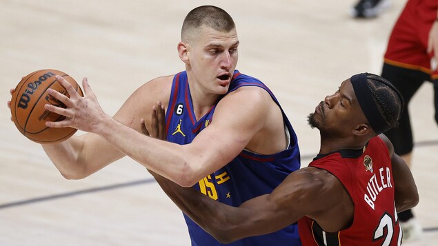 Un basketteur contrôle le ballon devant un adversaire qui le surveille étroitement.