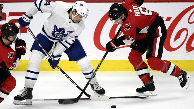 Deux joueurs des Maple Leafs de Toronto et des Sénateurs d'Ottawa luttent pour une rondelle lors d'un match.