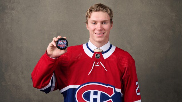 Un jeune homme vêtu d'un chandail avec le logo du Canadien de Montréaltient une rondelle de hockey dans sa main.