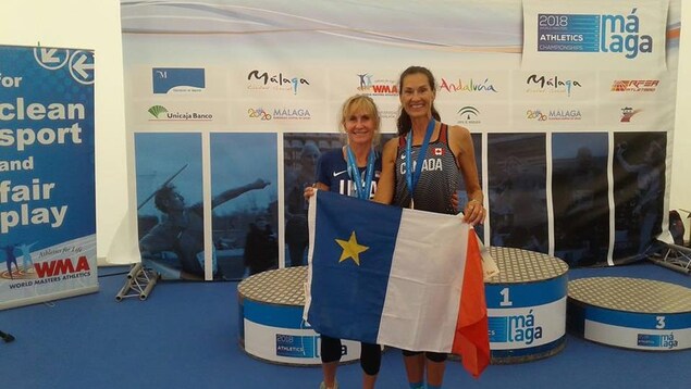 Patty Blanchard, à droite, et sa rivale Lesley Hinz, avec le drapeau acadien. Les deux dames ont leur médaille au cou. Patty Blanchard, à droite, et sa rivale Lesley Hinz, avec le drapeau acadien. Les deux dames ont leur médaille au cou.