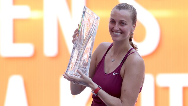Une joueuse de tennis sourit et tient un trophée.