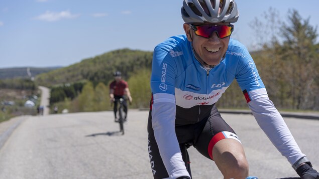 Il sourit à la caméra, sur son vélo.