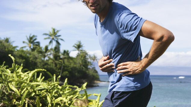 Un homme qui fait de la course à pied met ses mains sur son abdomen après avoir ressenti une crampe