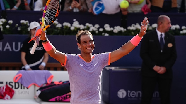 Le joueur de tennis lève les bras au ciel et sourit.