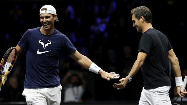 Un joueur de tennis sourit et félicite son partenaire de jeu en lui frappant la main durant un entraînement. 