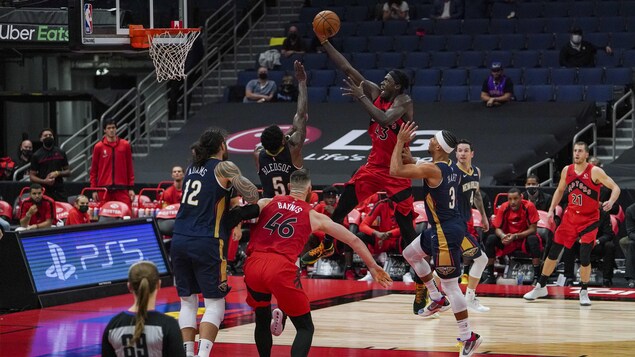 Un joueur de basketball tente d'inscrire un panier malgré la présence d'adversaires autour de lui.