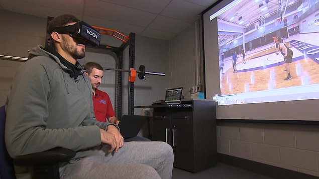 Un joueur de basketball assis regarde des séquences vidéo dans une lunette de réalité virtuelle dans un local de l'Université Bishop's à Sherbrooke.