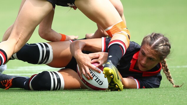 Une joueuse de rugby est au sol et tente de conserver la possession du ballon.