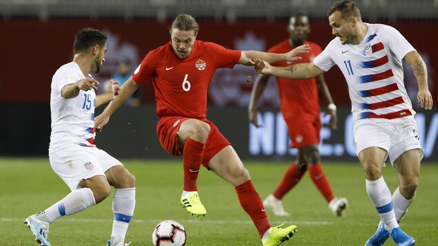Le milieu de terrain du Canada Samuel Piette contrôle le ballon entre deux joueurs américains lors d'un match de soccer à Toronto. 