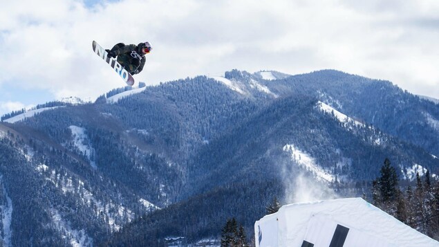 Toutant en plein saut devant une montagne enneigée.