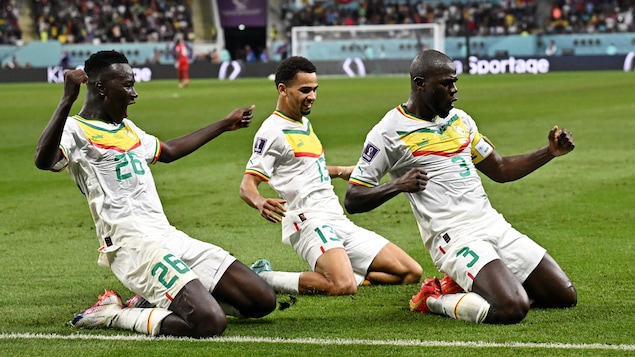 Trois joueurs sénégalais sont à genou sur le terrain  pour célébrer le but. 